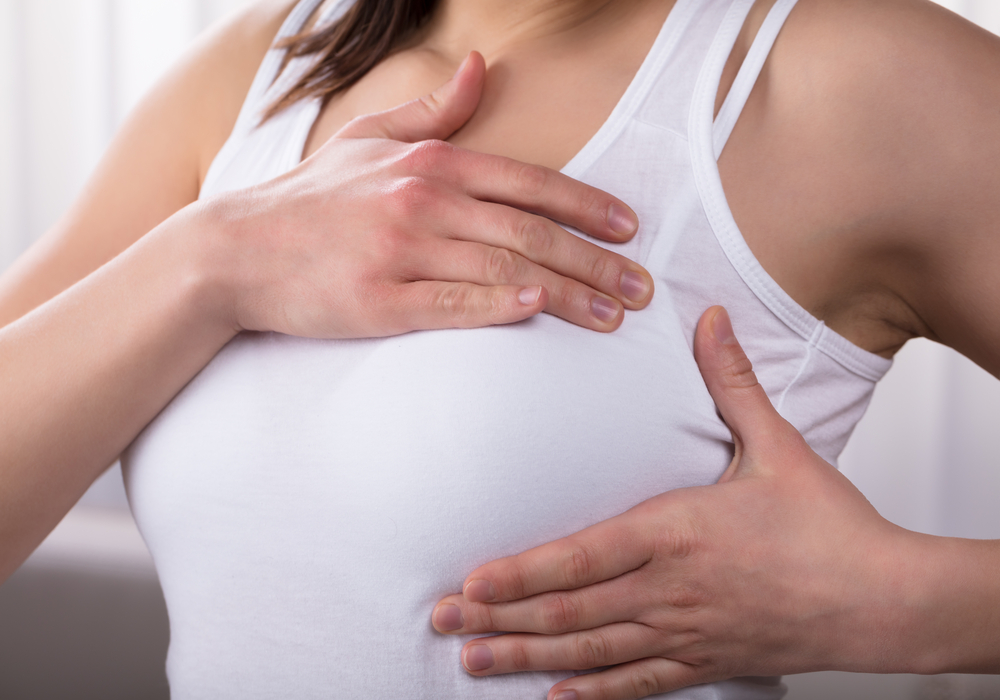 Woman holds her painful breast before her breast implant removal surgery